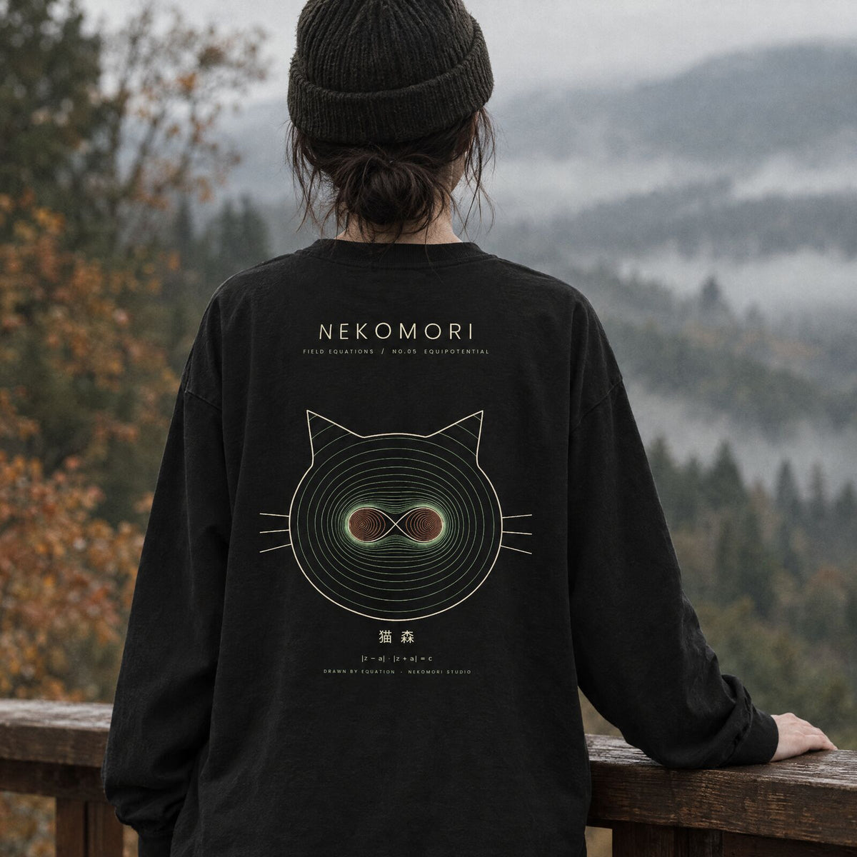 Generated mockup: a person seen from behind on a wooden balcony over a misty autumn valley, wearing the black Equipotential long sleeve tee with its cat face print on the back.