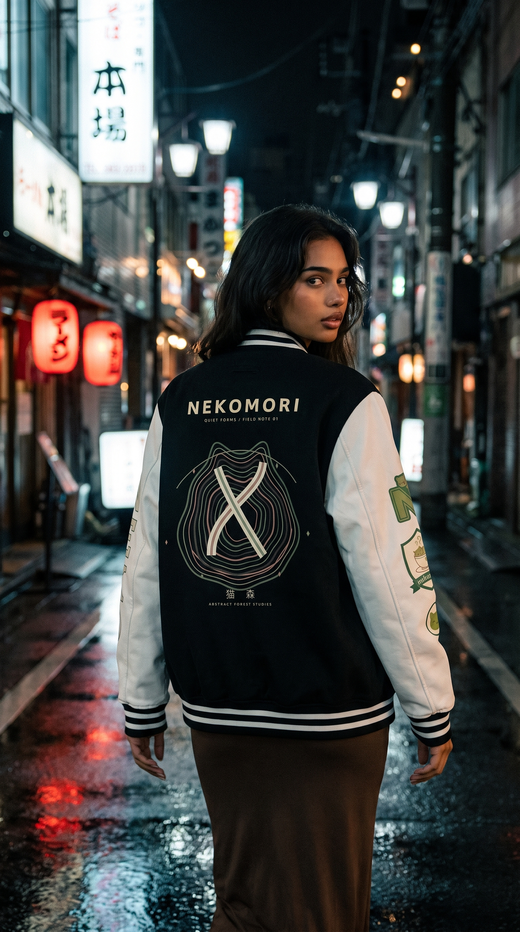 Model wearing the Nekomori Quiet Forms Field Note 01 letterman jacket in a city street setting at night.