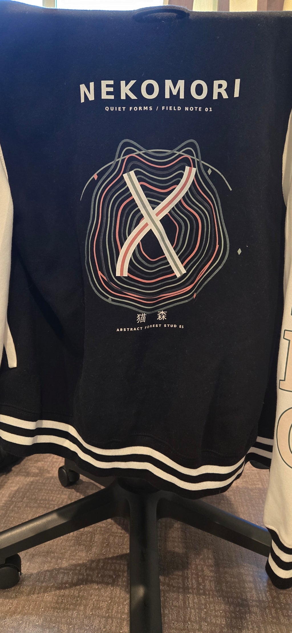 Real-life photograph of the Quiet Forms Field Note 01 letterman jacket, black body with white sleeves (photo 1 of 4).