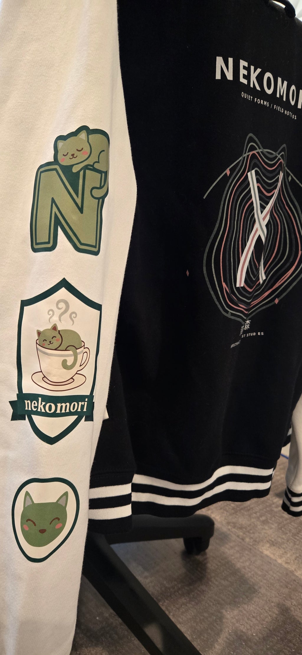 Real-life photograph of the Quiet Forms Field Note 01 letterman jacket, black body with white sleeves (photo 3 of 4).