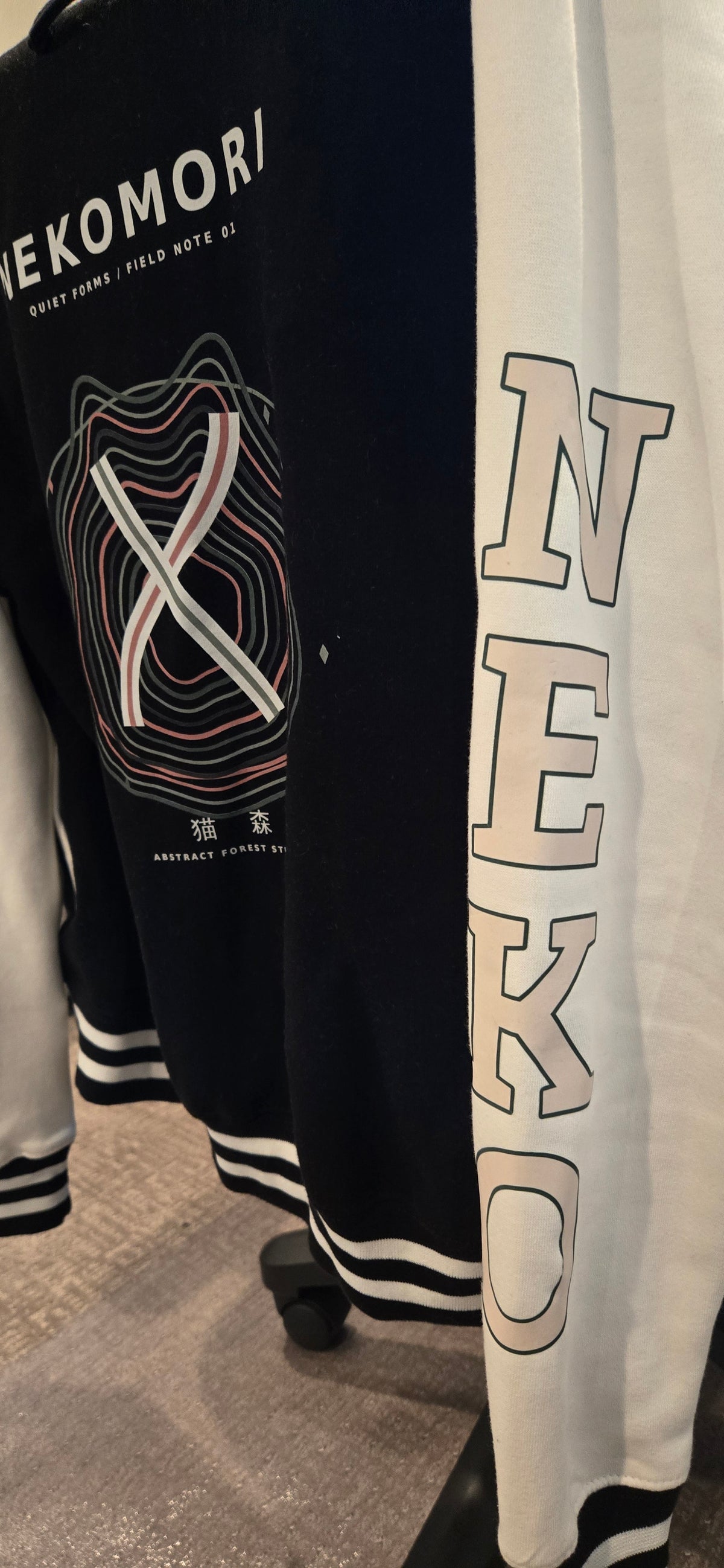 Real-life photograph of the Quiet Forms Field Note 01 letterman jacket, black body with white sleeves (photo 2 of 4).